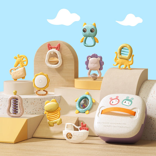 Aesthetic display of a baby rattle and teether toy set arranged on pastel-toned platforms with a blue sky and clouds background. The set includes 12 colorful toys shaped like animals and objects—such as a giraffe, frog, turtle, lion, boat, and more—alongside a storage box with an orange handle. Designed for sensory play, shaking, teething, and grasping.