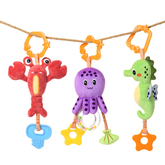 Three colorful plush sea animal toys — a red lobster with a blue teether, a purple octopus with dangling textured rings and star-shaped teethers, and a green seahorse with wings and an orange teether — hanging on an orange clip from a rope, designed for babies' sensory and motor skill development.