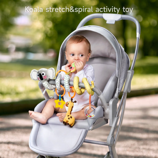 Baby sitting in a stroller playing with a Koala-themed stretch and spiral activity toy wrapped around the stroller bar, featuring hanging plush toys including a bird, giraffe, star-shaped teether, and rattle ring to stimulate sensory development.