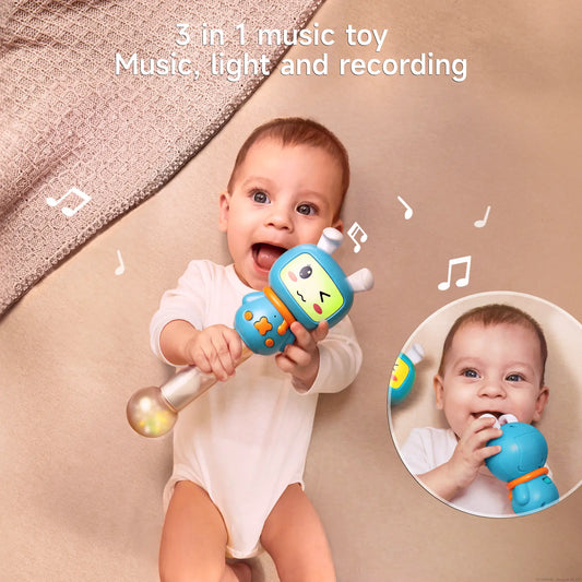 Baby lying on a beige bed holding a blue bunny-shaped musical rattle with light-up handle and teether ears. The baby is smiling and playing with the toy, surrounded by floating musical notes. A small inset shows the baby chewing on the toy’s bunny ears.