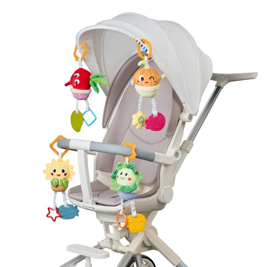 White baby stroller decorated with four colorful plush hanging toys shaped like a beetroot, onion, sunflower, and cabbage. Each toy features cheerful embroidered faces and dangling textured teethers in fun shapes like stars, leaves, and animals.