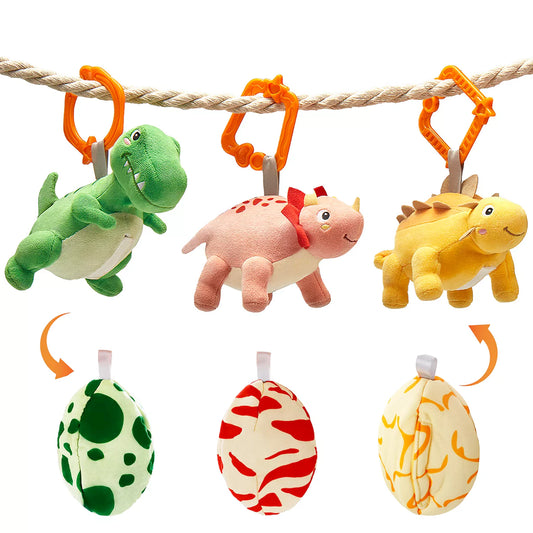 Three reversible plush dinosaur toys hanging by orange clips, featuring green, pink, and yellow dinosaurs that fold into matching patterned eggs