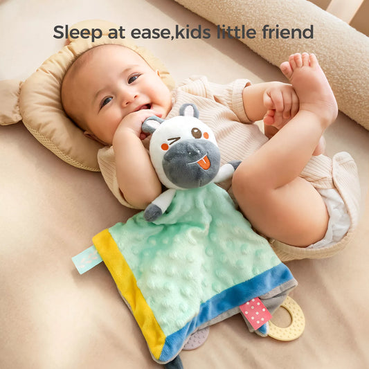 Smiling baby lying on a bed, holding a cute zebra baby security blanket with soft textured fabric and teething rings