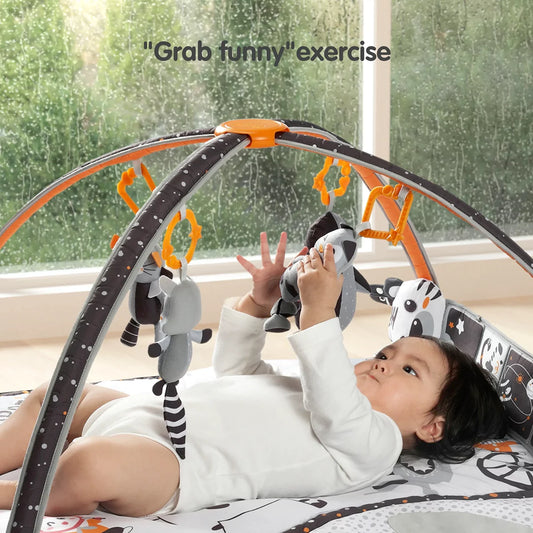 Baby lying on a black and white baby play gym with orange accents, playing with hanging rattles shaped like animals, designed to stimulate visual and motor development.
