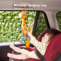 Baby sitting in a car seat, reaching for a plush giraffe toy hanging from the car's grab handle using an orange hanging ring. The toy includes colorful teething rings, crinkle textures, and rattle elements. Text at the top reads “Portable hanging ring,” highlighting its easy attachment for travel use.
