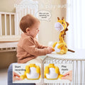 A baby sitting at a table interacting with a yellow giraffe plush toy that can record and play audio; the toy features labeled buttons for recording and playing music.
