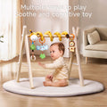 Baby sitting on a round play mat reaching for a giraffe-themed spiral activity toy hanging from a wooden play gym, featuring plush animal and tree figures designed to stimulate cognitive development and soothe the baby.