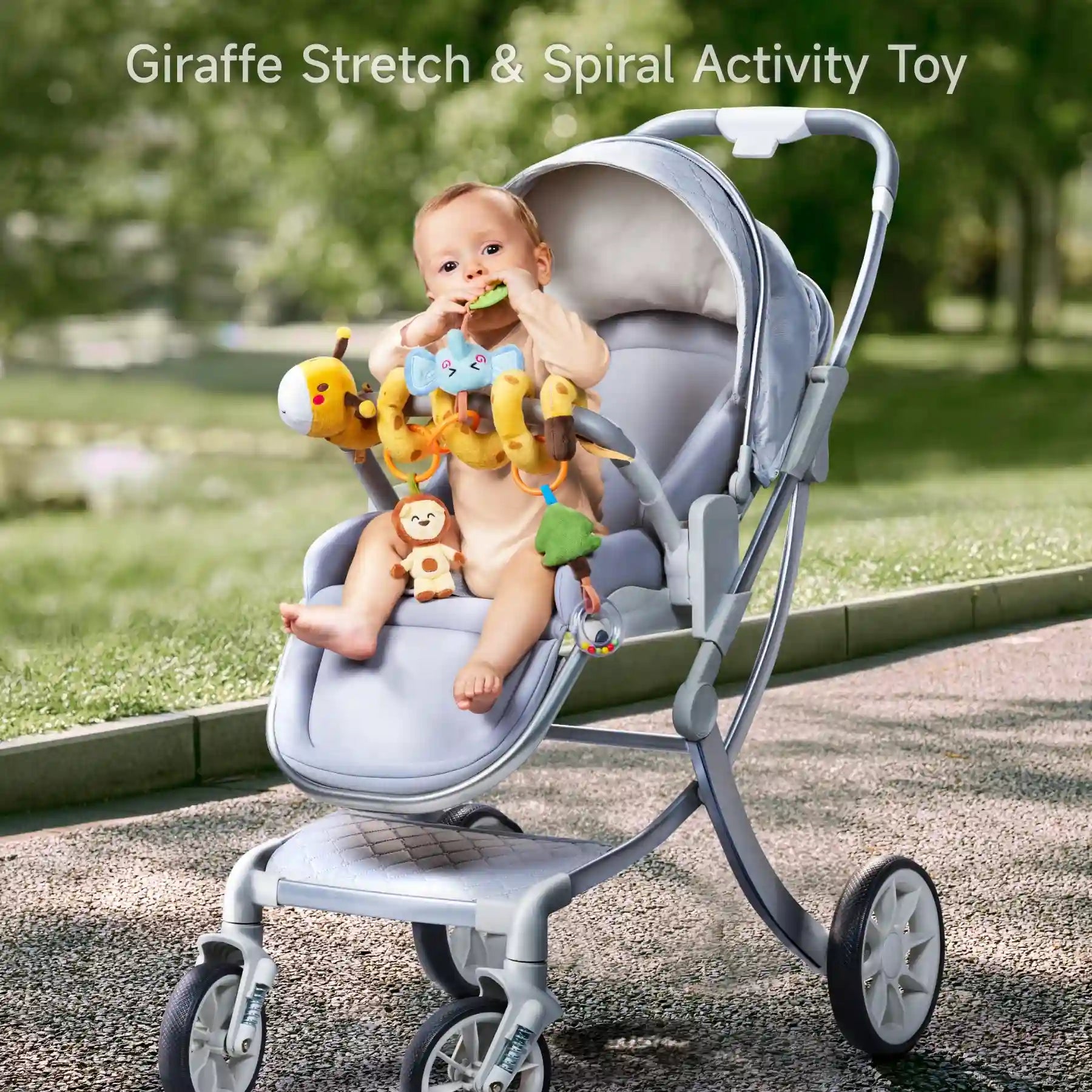 Baby sitting in a gray stroller playing with a plush giraffe spiral activity toy attached to the front bar. The toy includes hanging elements like a blue elephant, green tree, lion, and rattle to encourage sensory and motor skills development.