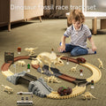 Young boy playing on the floor with a dinosaur fossil racetrack set that includes large skeletal dinosaur figures, two toy cars, bridges, signs, and fossil accessories on a beige carpet in a cozy indoor setting.