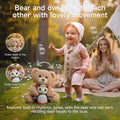 A teddy bear and owl plush toy sit on the grass while nodding their heads to the rhythm. A smiling toddler plays nearby outdoors with a tent and parent in the background, showcasing the toy’s interactive singing feature in a joyful setting.