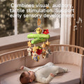 A baby lying in a crib looks up at a Woodland Animal Crib Mobile hanging above. The mobile features a green tree branch design with a plush bee and red flower on top, and hanging plush toys including stars, a ladybug, an owl, a strawberry, a sloth, and a raccoon. Musical notes are illustrated around the mobile, and text on the image reads, 